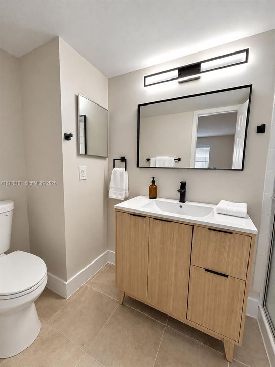 Modern light wood-finish vanity with a rectangular integrated sink, neutral stone-composite countertop, matte black faucet, and matching framed mirror with integrated LED light fixture