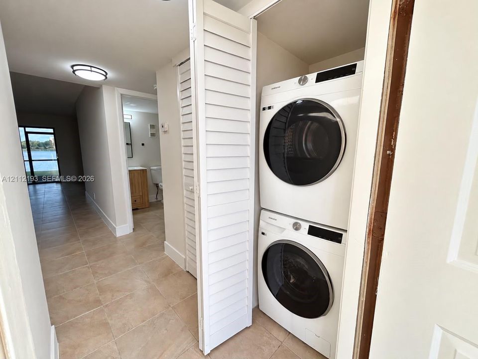 Stacked laundry appliance set housed within a closet featuring white louvered doors