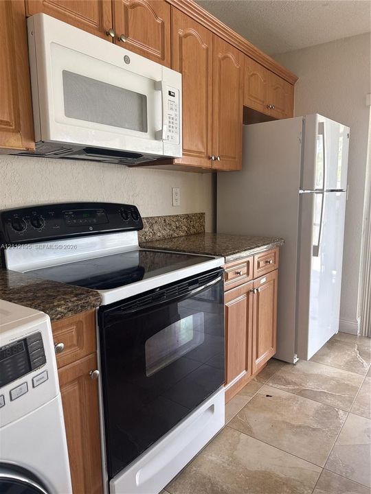 Kitchen featuring shaker-style wood cabinetry, stone-surface countertops, built-in white appliances, and tile flooring