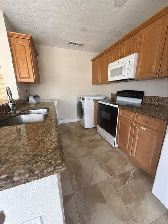 Kitchen featuring wood cabinetry, stone-finish countertops, tile flooring, dual-basin stainless steel sink, and built-in appliances