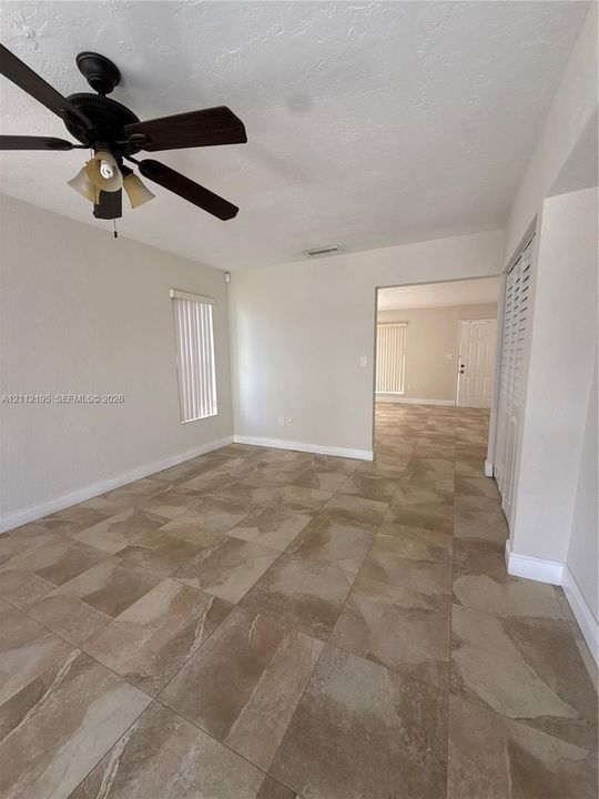 Large-format neutral tile flooring throughout with a multi-light ceiling fan and louvered-style closet doors