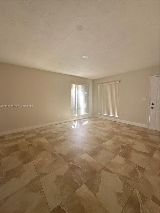 Neutral-toned interior space featuring large-format ceramic tile flooring, two windows with vertical blinds, and a recessed ceiling light fixture