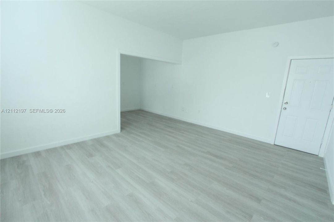 Interior space featuring light-toned wood-finish flooring, smooth wall surfaces, and a panel-style door with metallic hardware
