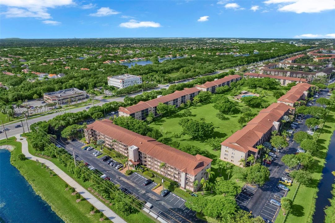 Aerial perspective of a multi-story residential complex featuring tile roofing, surface parking areas, and expansive landscaped green spaces