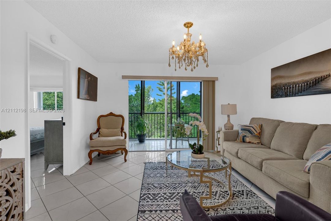 Ceramic tile flooring, ornate crystal-style chandelier, and sliding glass doors opening to a private balcony with black metal railing