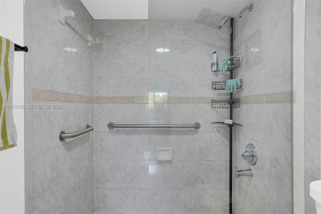 Shower stall featuring floor-to-ceiling tile surround with decorative accent banding, built-in recessed soap niche, stainless steel grab bars, and rain-style shower head with temperature control valve