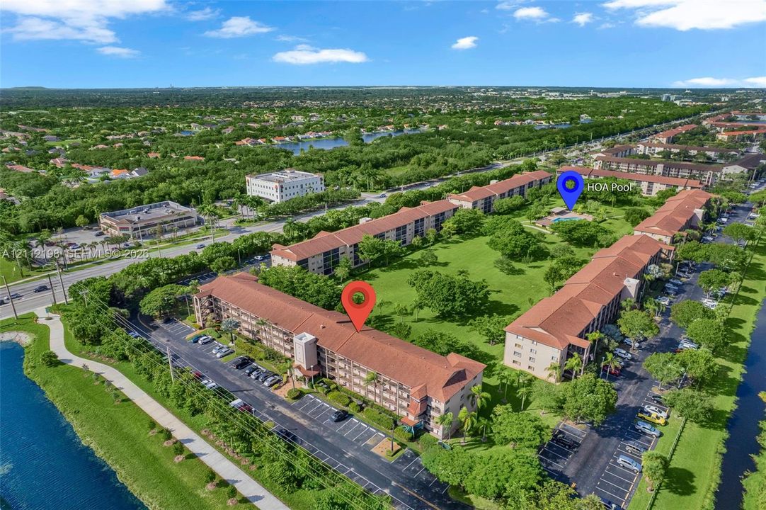 Multi-story residential complex featuring tile roofing, surface parking areas, manicured green space, and a community swimming pool