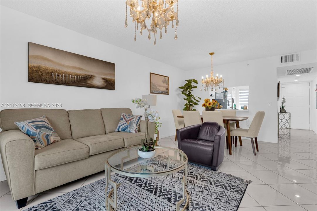 Open-concept living space featuring high-gloss tile flooring, two ornate multi-tiered crystal chandeliers, and a service pass-through window