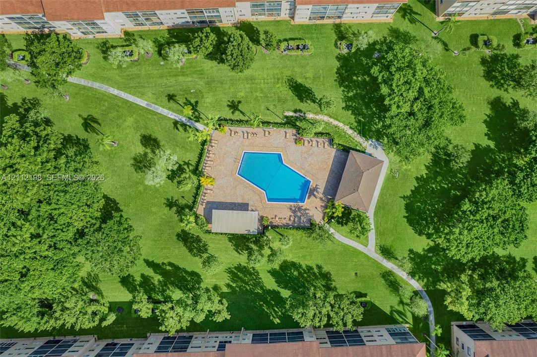 Community pool with stone-paver deck, covered pavilion, mature landscaping, and paved pedestrian walkways
