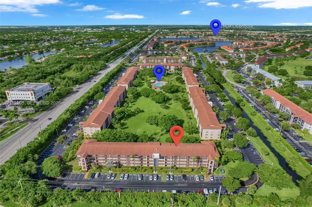 Aerial view of the multi-story residential complex featuring a central courtyard with mature trees, paved parking areas, a swimming pool, and an onsite clubhouse
