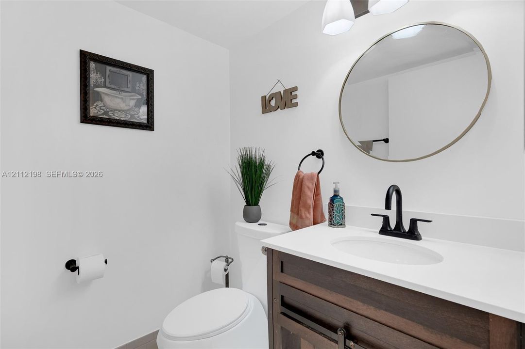 Vanity featuring a dark wood-finish cabinet, white surface, and matte black faucet, paired with a circular wall mirror and dual-light fixture