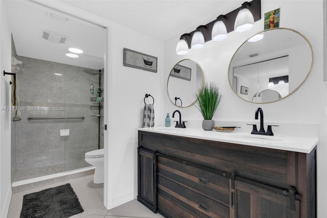 Dual-sink vanity featuring a dark wood-finish cabinet with sliding barn-style doors, stone-surface countertop, matte black faucets, and circular mirrors
