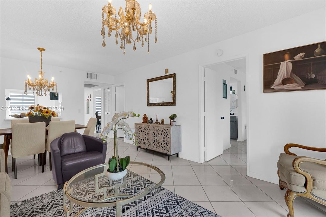 Open-concept interior featuring light-toned tile flooring, two decorative crystal chandeliers, and a wall-mounted framed mirror