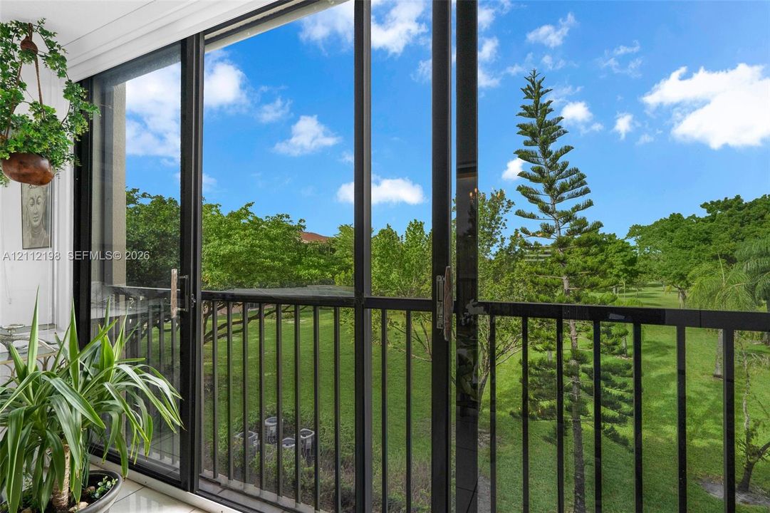 Full-height glass sliding doors with black frames and integrated metal balustrades, opening to an expansive green space featuring mature trees and manicured lawns