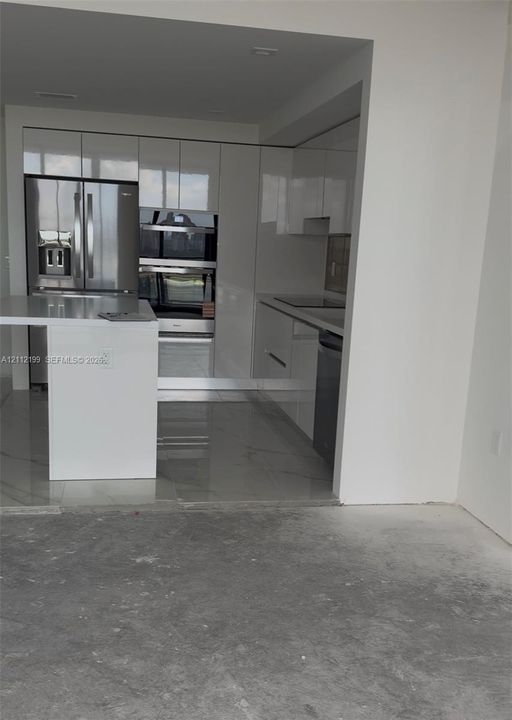 Kitchen featuring high-gloss cabinetry, stone-surface countertops, an integrated island, built-in stainless steel appliances, and tile flooring