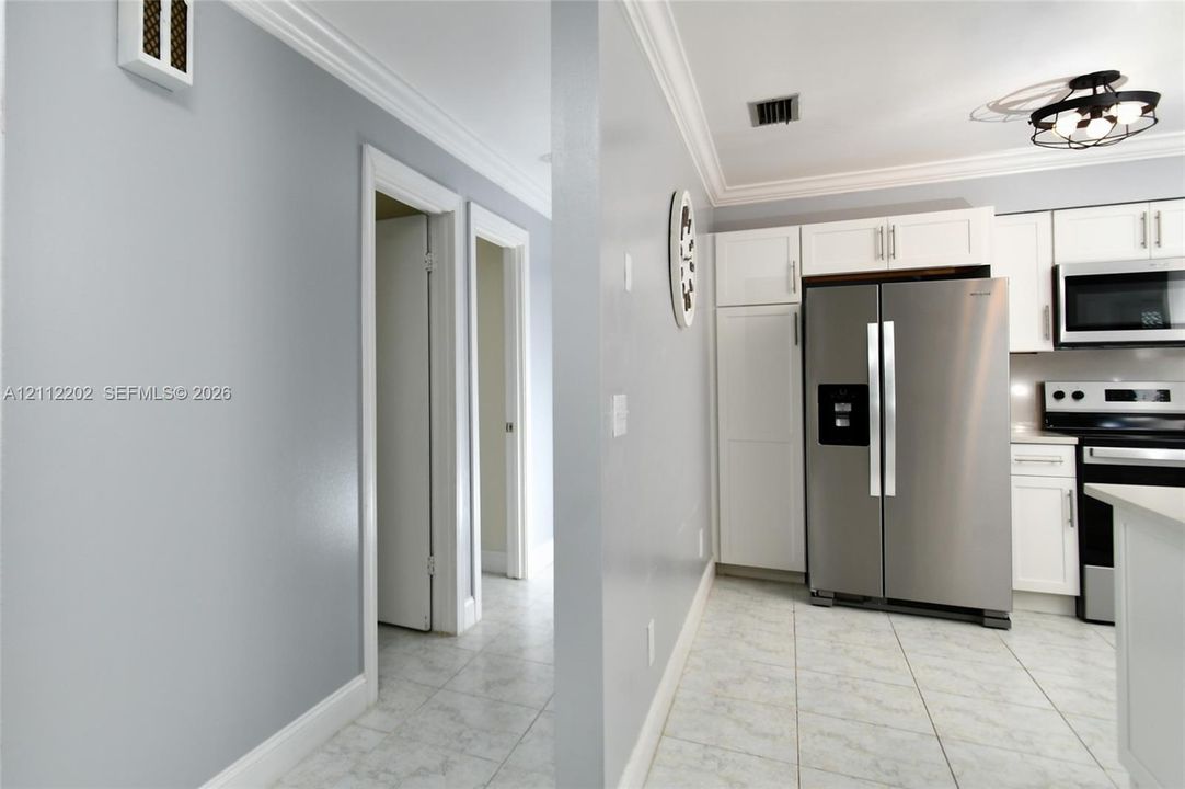 Kitchen featuring white shaker-style cabinetry, stainless steel appliances, tiled flooring, and crown molding