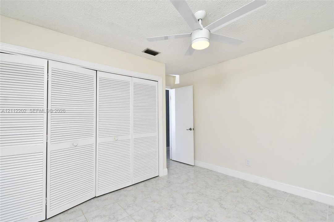 Room featuring four-panel louvered closet doors, neutral wall finish, light-toned ceramic tile flooring, and a white ceiling fan with an integrated light fixture