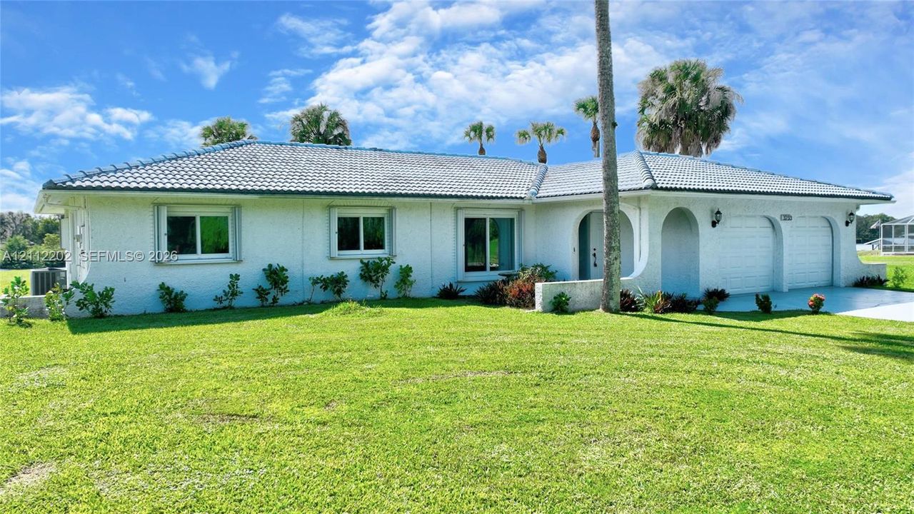 Single-story exterior featuring white stucco siding, a grey tile roof, arched entryway, and an attached two-car garage