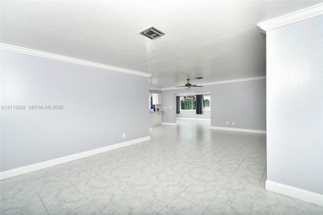Open-concept interior featuring neutral wall tones, large-format tile flooring, crown molding, and a ceiling fan