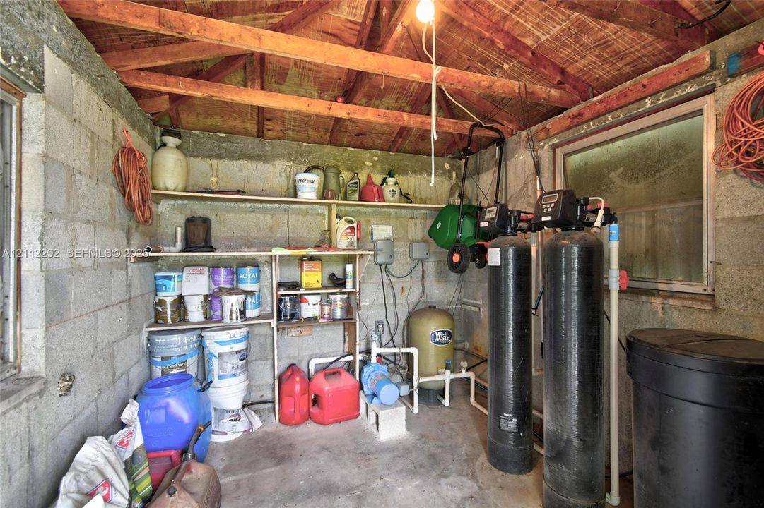 Utility space featuring exposed beam ceiling, concrete block walls, built-in open shelving, and integrated water filtration system