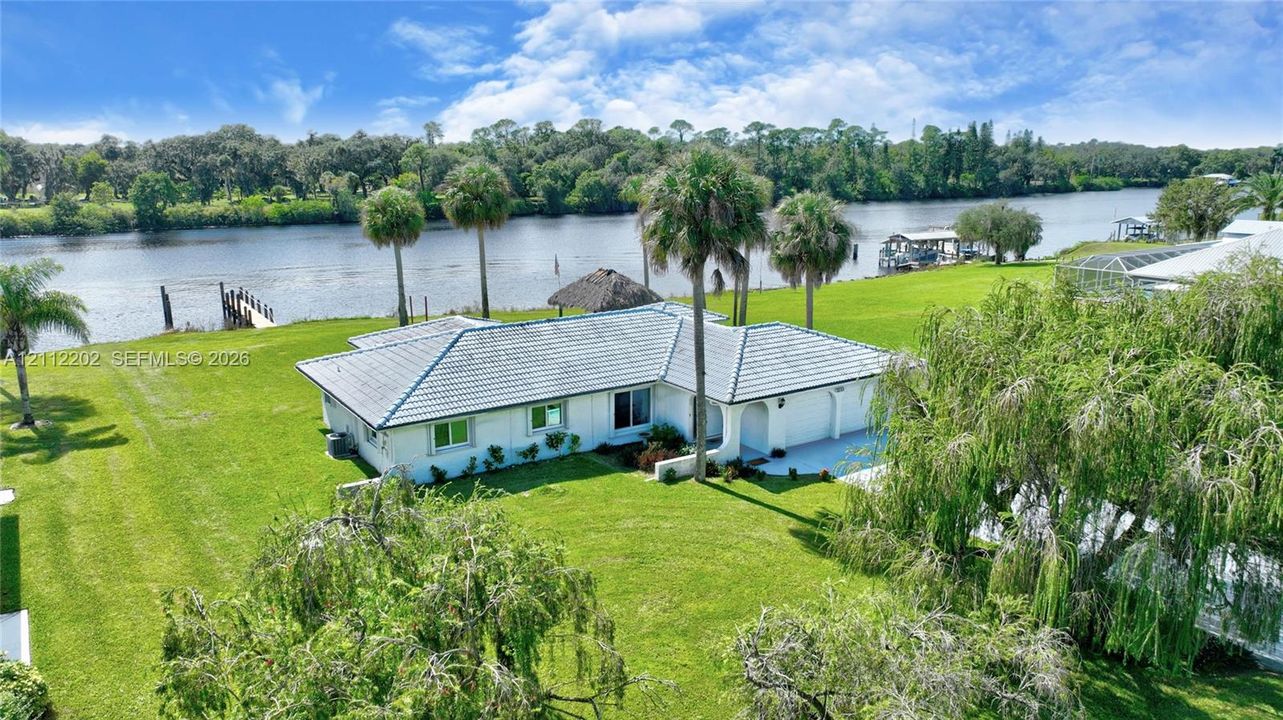 Waterfront property featuring a tile roof, expansive lawn, mature palm trees, and a private dock