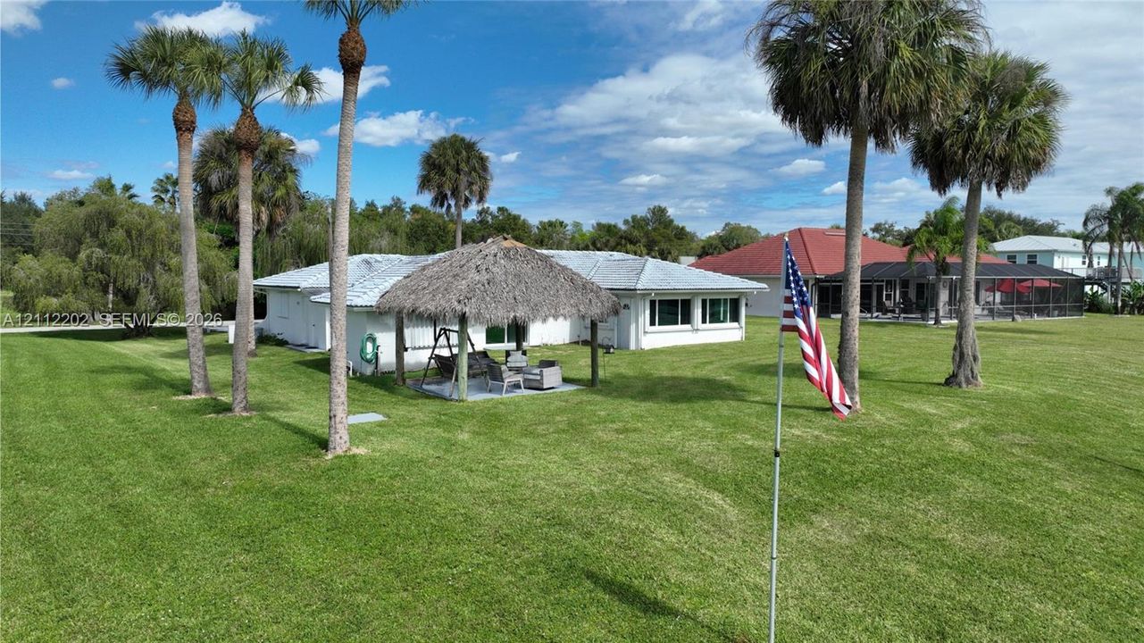 Expansive manicured lawn featuring mature palm trees and a permanent tiki-style thatched-roof structure