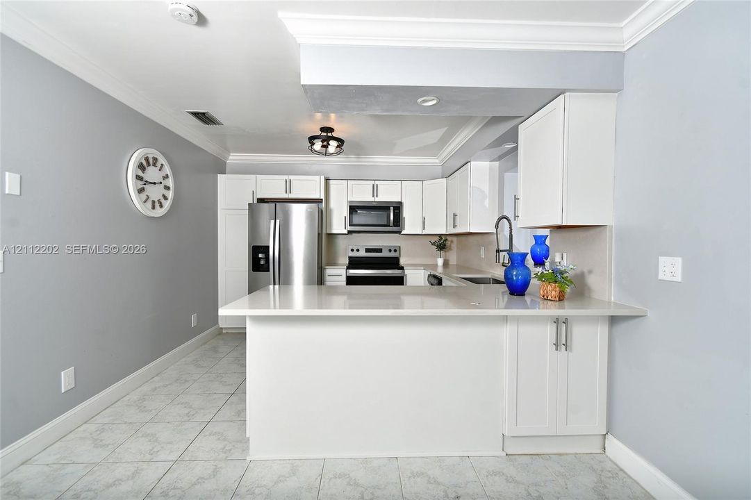 Kitchen featuring white cabinetry, quartz countertops, stainless steel appliances, tile flooring, and crown molding