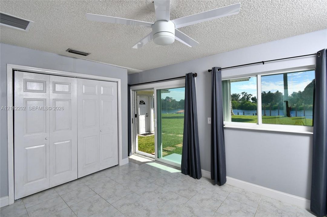 Room interior featuring light-toned tile flooring, a multi-panel sliding glass door, a double-door reach-in closet, and a ceiling-mounted light fixture with fan blades