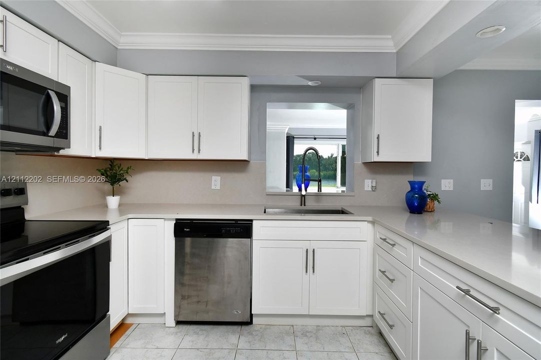 Kitchen featuring white Shaker-style cabinetry, stone-finish countertops, stainless steel appliances, a deep undermount sink with a high-arch faucet, and crown molding