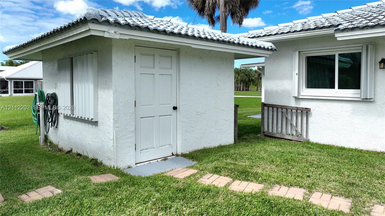 Stucco exterior featuring a tiled roof, six-panel entry door, and a stone paver walkway set within a grass lawn