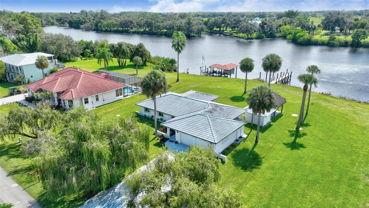 Waterfront property featuring a private boat dock, sprawling lawn, mature palm trees, and a multi-car garage