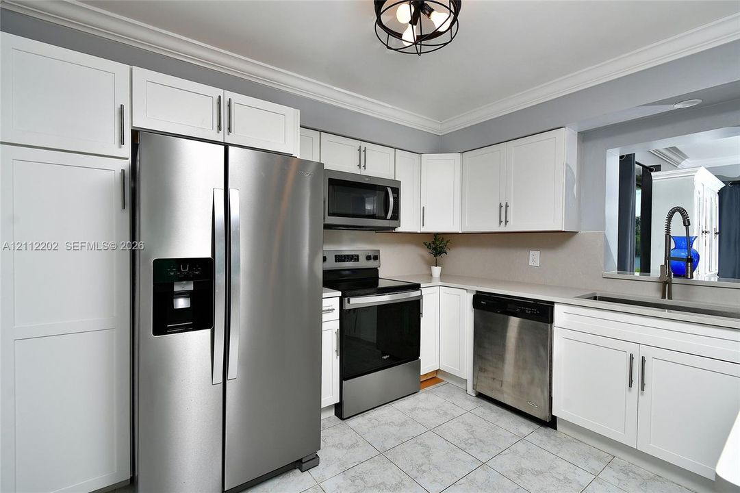 Kitchen featuring white cabinetry, stainless steel appliances, tile flooring, stone-finish countertops, and a ceiling-mounted industrial-style light fixture