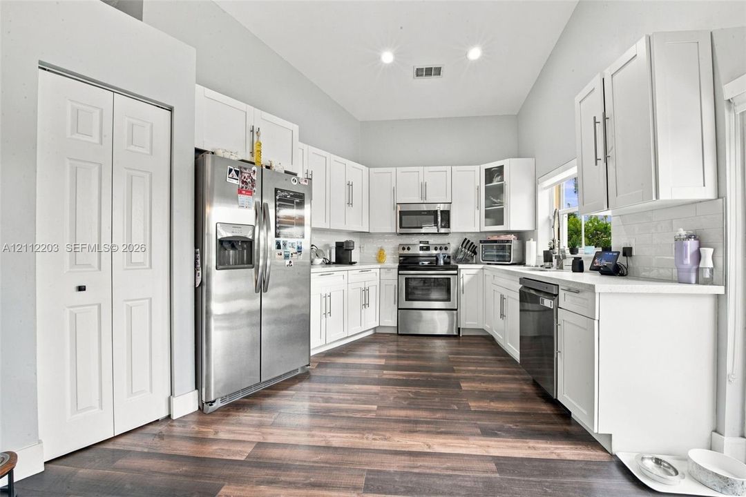 Kitchen featuring white shaker-style cabinetry, stainless steel appliances, white subway tile backsplash, solid-surface countertops, and wood-finish flooring