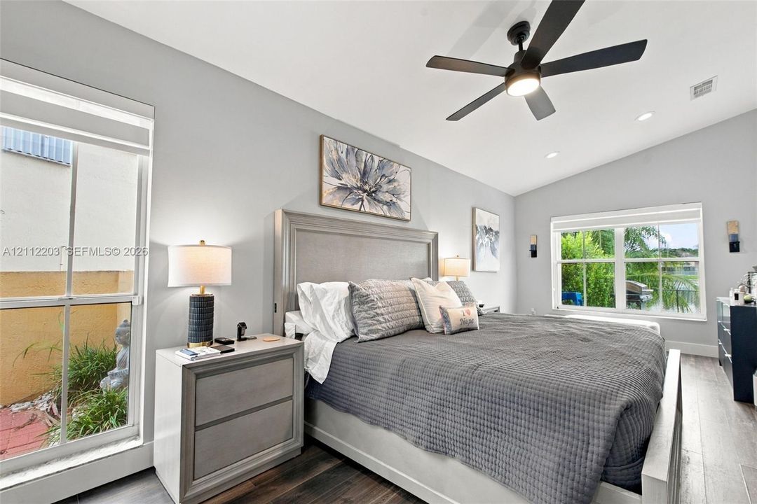 Vaulted ceilings, wood-finish flooring, recessed lighting, matte black ceiling fan, and large windows with multi-pane glazing