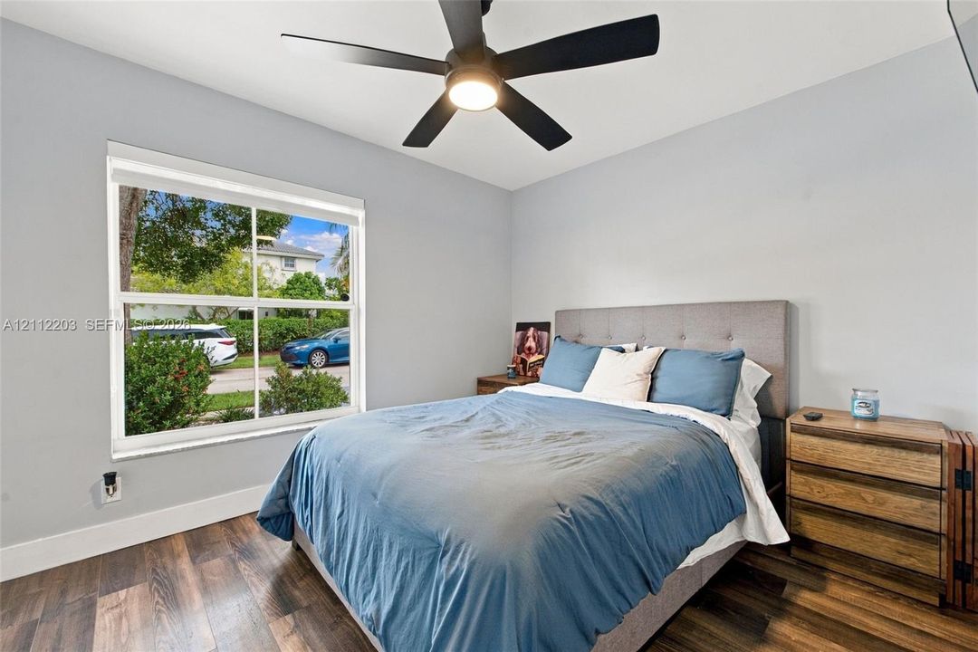 Room featuring wood-finish flooring, a matte black multi-blade ceiling fan with integrated lighting, and a large single-hung window