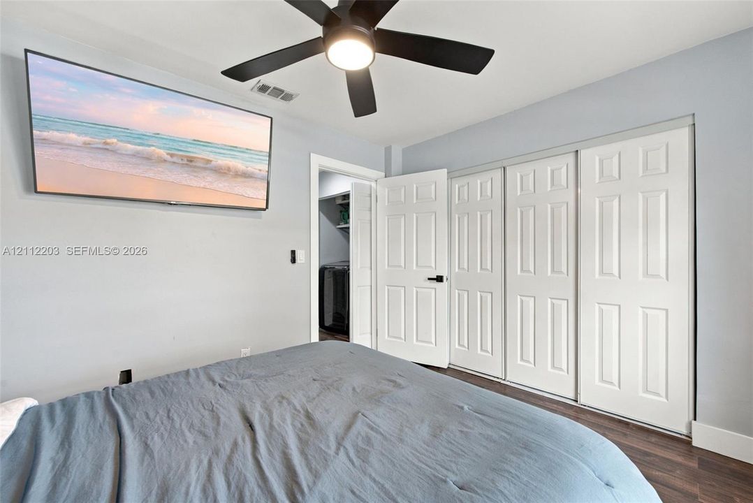 Neutral-toned interior featuring wood-finish flooring, a contemporary matte black ceiling fan with integrated lighting, and white six-panel closet doors with matching matte black hardware