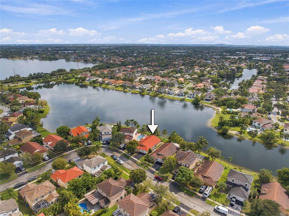 Aerial perspective of a waterfront property featuring a multi-slope roof, private swimming pool, and concrete driveway