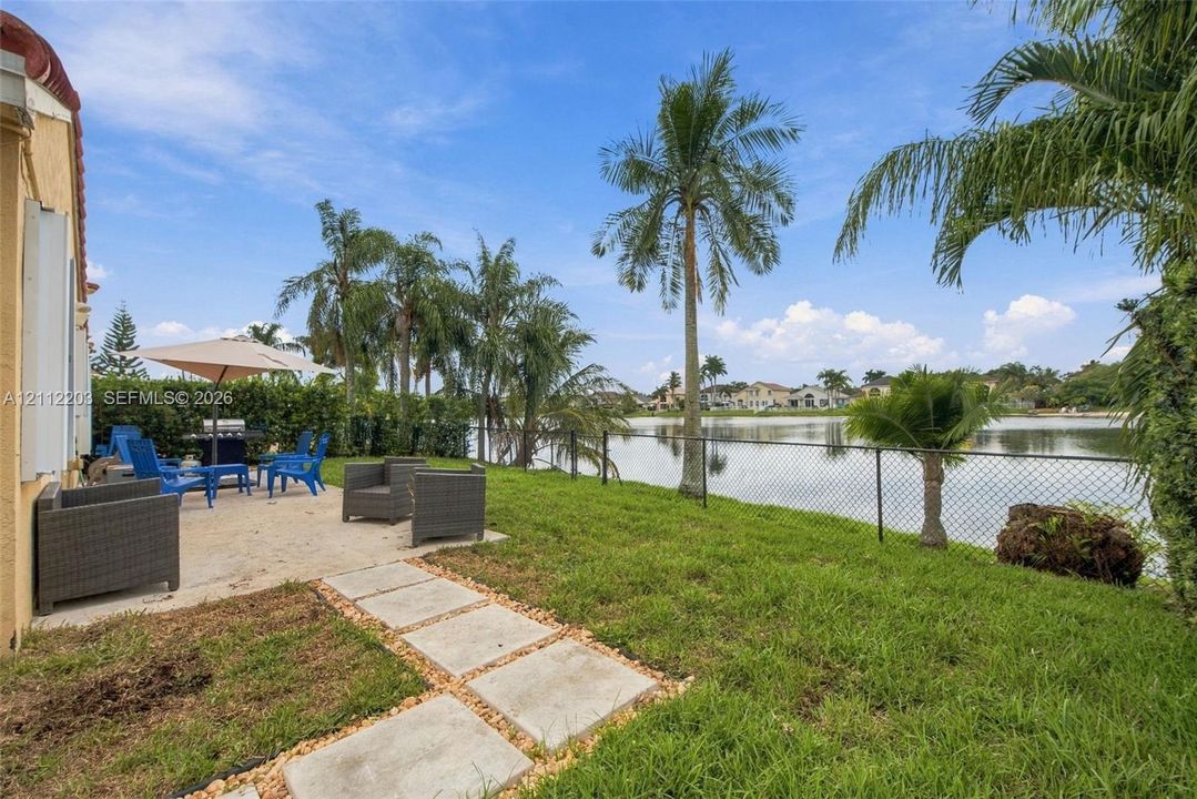 Backyard featuring a paved patio, concrete paver path, water frontage, metal perimeter fencing, and mature palm trees