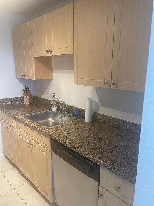 Light-toned cabinetry, speckled stone-finish countertops, stainless steel sink with metal faucet, integrated dishwasher, and ceramic tile flooring