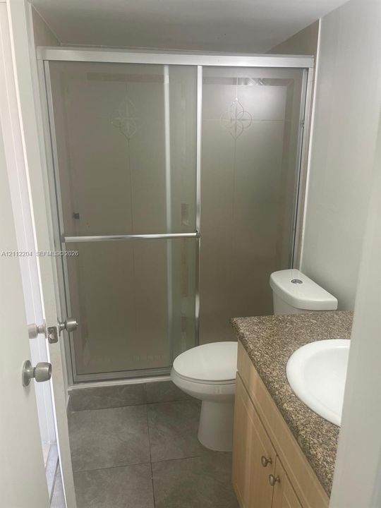 Bathroom featuring a shower stall with a sliding glass door, vanity with a stone-finish countertop, and integrated sink