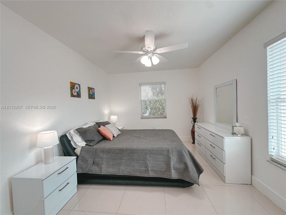 Spacious room featuring neutral tile flooring, a multi-blade ceiling fan with integrated lighting, and multiple windows fitted with horizontal blinds