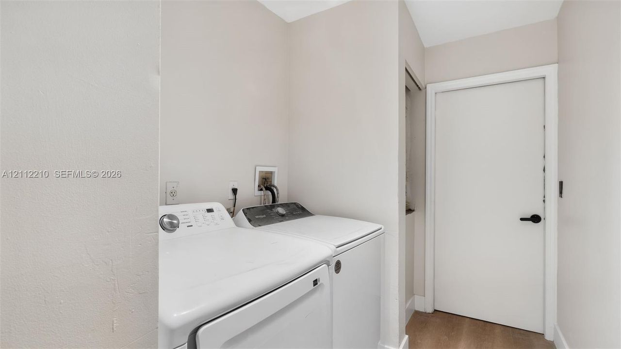Dedicated laundry space featuring neutral wall paint, wood-finish flooring, and a solid-core interior door with matte black hardware