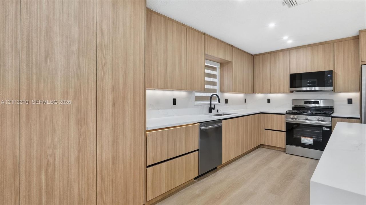 Kitchen featuring flat-panel wood-finish cabinetry, white solid-surface countertops, full-height tile backsplash, stainless steel appliances, and wood-finish flooring