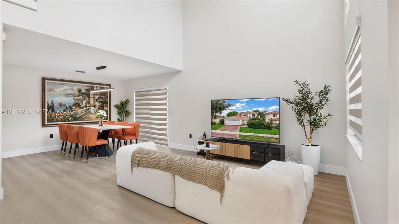 High-ceiling living area featuring wood-finish flooring, neutral wall paint, and horizontal zebra blinds