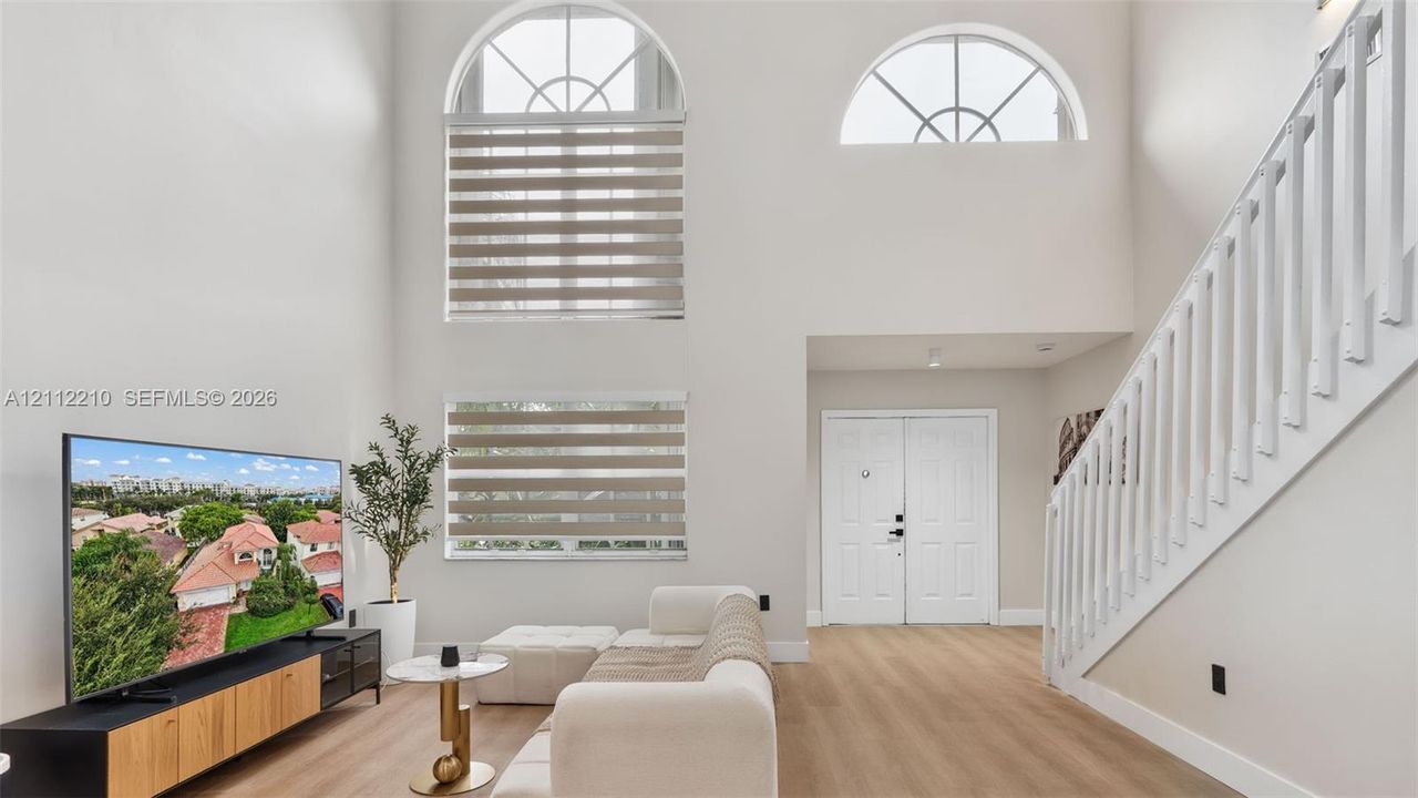 Double-height ceilings, arched upper windows, wood-finish flooring, staircase with white vertical balusters, and double-door entry