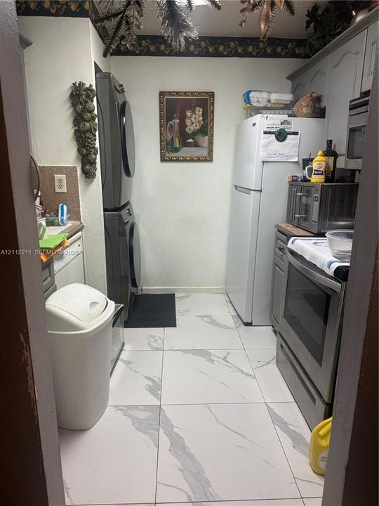 Large-format stone-style tile flooring featuring high-contrast veining, vertical stacked laundry unit, white refrigerator, and stainless steel oven range with built-in cabinetry