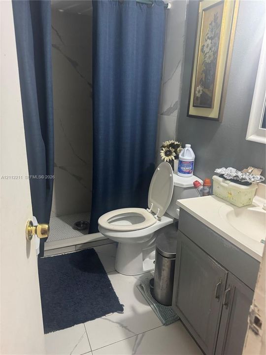 Bathroom featuring a vanity with a white countertop, large-format tile flooring, and a walk-in shower with stone-patterned wall tiling