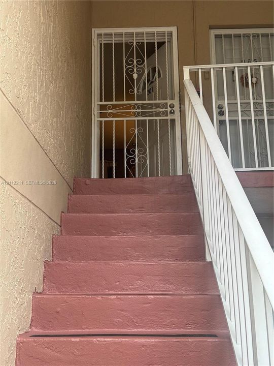 Stucco exterior staircase with painted concrete steps and metal railing featuring decorative security gates