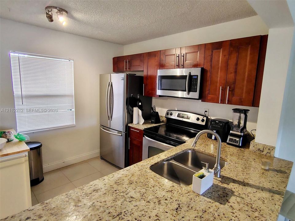 Kitchen featuring cherry-finish cabinetry, stone countertops, stainless steel appliances, and a dual-basin undermount sink with a high-arch faucet