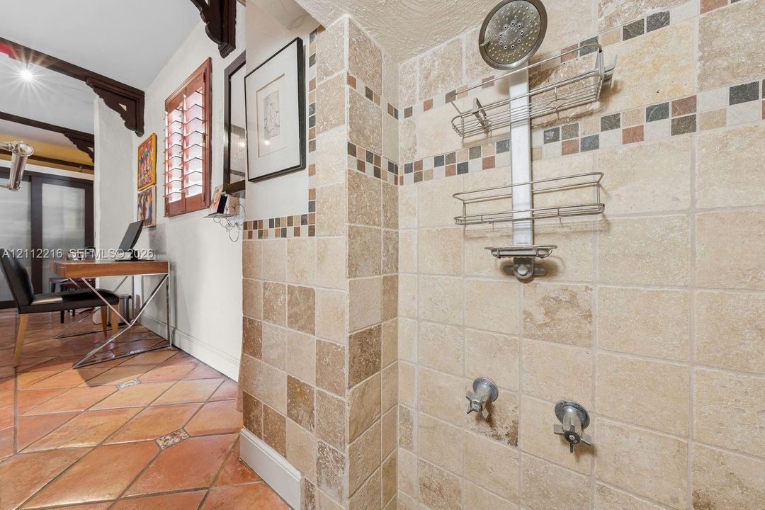 Shower stall featuring square-cut natural stone wall tile, decorative mosaic accent banding, a chrome-finish shower head, and dual-handle wall-mounted faucets